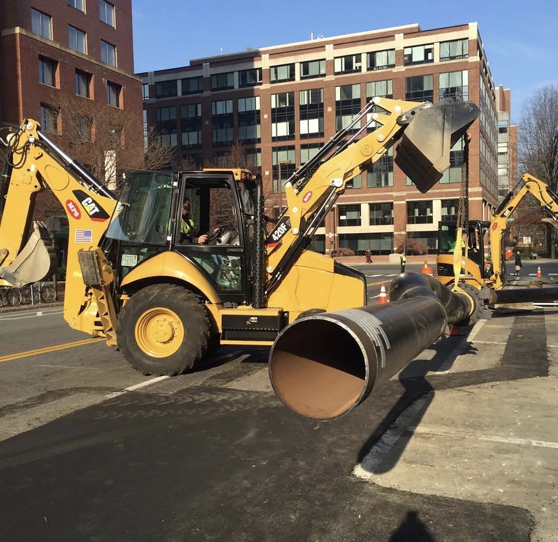 Mass Pipeline Services backhoe setting large-diameter pipe during underground utility installation